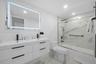 Modern bathroom featuring a double-sink vanity with matte black hardware, backlit LED mirror, recessed ceiling lighting, and a bathtub-shower combinat