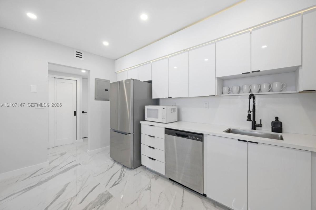 Kitchen featuring white high-gloss cabinetry, stainless steel appliances, solid-surface countertops, a matte black pull-down faucet, and polished ston