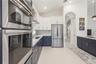 Kitchen featuring dual-tone cabinetry, stainless steel appliances, quartz countertops, mosaic tile backsplash, and large-format tile flooring