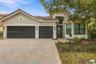 Stucco exterior with a tiled roof, paver driveway, three-car garage, and multi-pane windows
