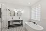 Double vanity with matte black hardware, freestanding soaking tub, walk-in glass-enclosed shower, patterned floor tile, and glass block window