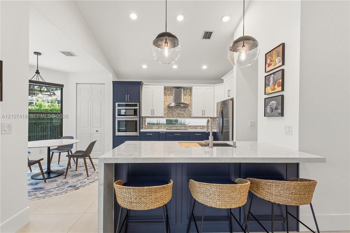 Kitchen featuring a central island with a solid surface countertop, contrasting navy and white cabinetry, a built-in double wall oven, patterned tile 