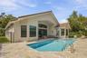 Rear exterior featuring a tile roof, stucco siding, stone paver decking, and a built-in swimming pool