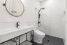 Wall-mounted round mirror, console-style vanity with a rectangular sink, matte black faucet hardware, glass-enclosed shower with subway tile surround,