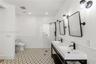 Dual vanity with rectangular sinks, matte black fixtures, framed mirrors, glass-enclosed shower, and geometric patterned tile flooring