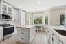 Kitchen featuring white shaker-style cabinetry, wood-top center island, stone-surfaced countertops, stainless steel appliances, and wood-finish floori