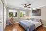 Room featuring wood-finish flooring, dual windows with roller shades, ceiling fan with integrated lighting, and multi-panel closet doors