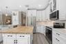 Kitchen featuring white shaker-style cabinetry, wood-top center island, stainless steel appliances, light-toned countertop surfaces, and wood-finish f
