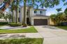 Two-story residence featuring a light-toned exterior, concrete tile roof, multi-car garage, and landscaped front grounds with mature palm trees