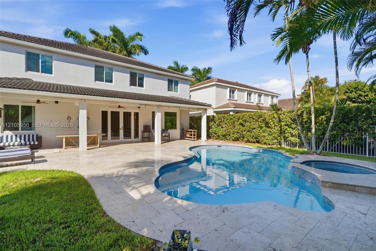 Covered concrete patio with multi-panel glass doors, stone-tiled pool deck, and an integrated spa