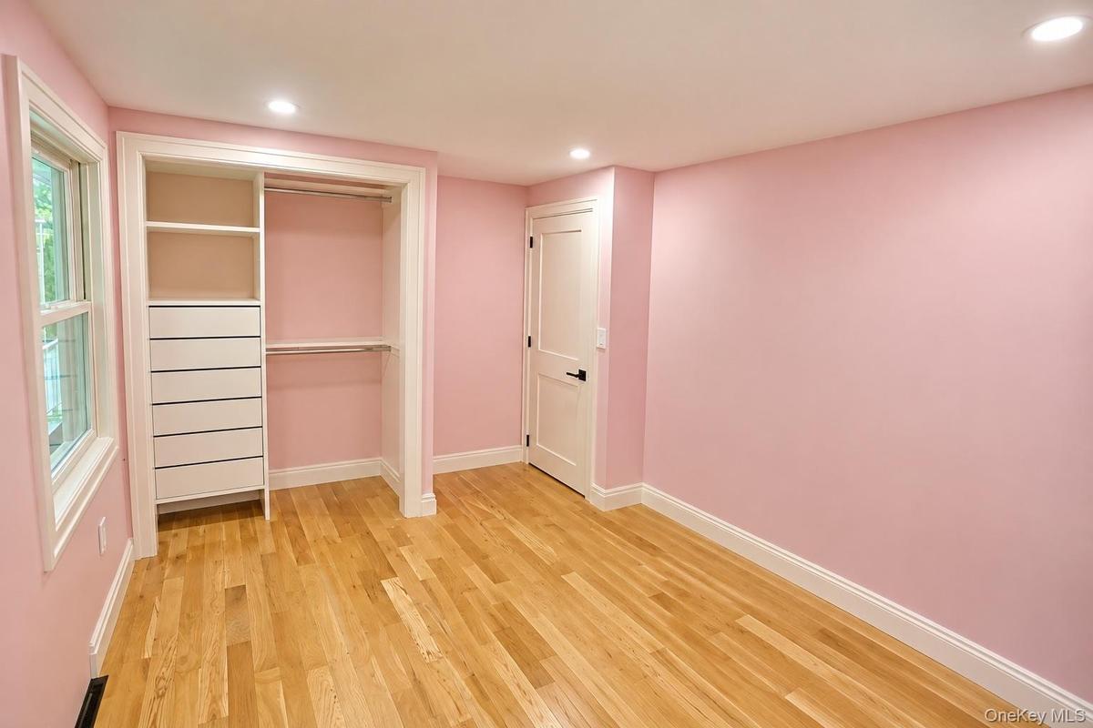 Interior space featuring wood-finish flooring, built-in closet organization with integrated drawer storage, a two-panel interior door with matte black