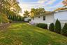 Rear exterior featuring white siding, a concrete patio, tiered retaining walls, a lattice-top fence, and mature landscaping