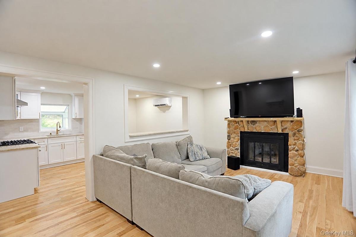 Living area featuring light wood-finish flooring, recessed lighting, and a floor-to-ceiling river stone fireplace