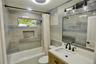 Bathroom featuring large-format neutral-toned wall tile, wood-finish vanity with light-colored solid surface countertop, integrated shower niche, and 