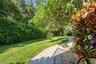 Expansive backyard featuring a brick paver walkway, manicured lawn, established landscaping, and mature trees