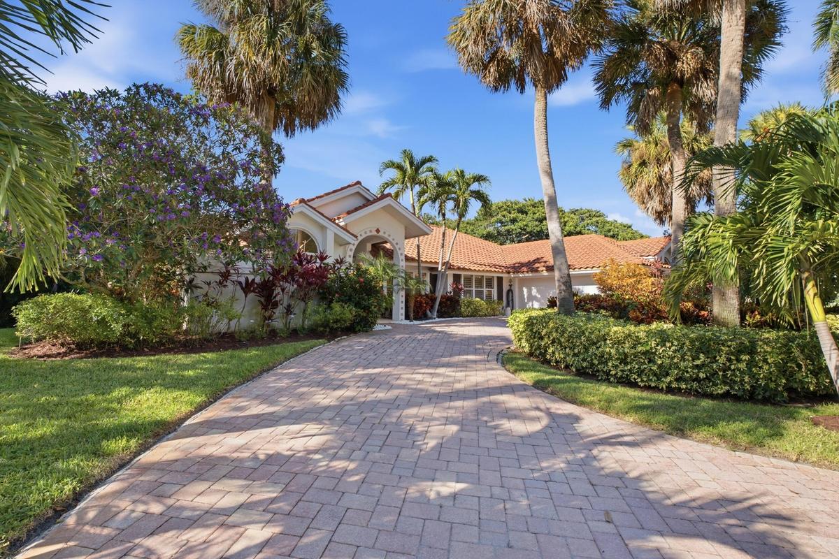 Exterior featuring a curved paver driveway, tile roof, arched entryway, and mature tropical landscaping