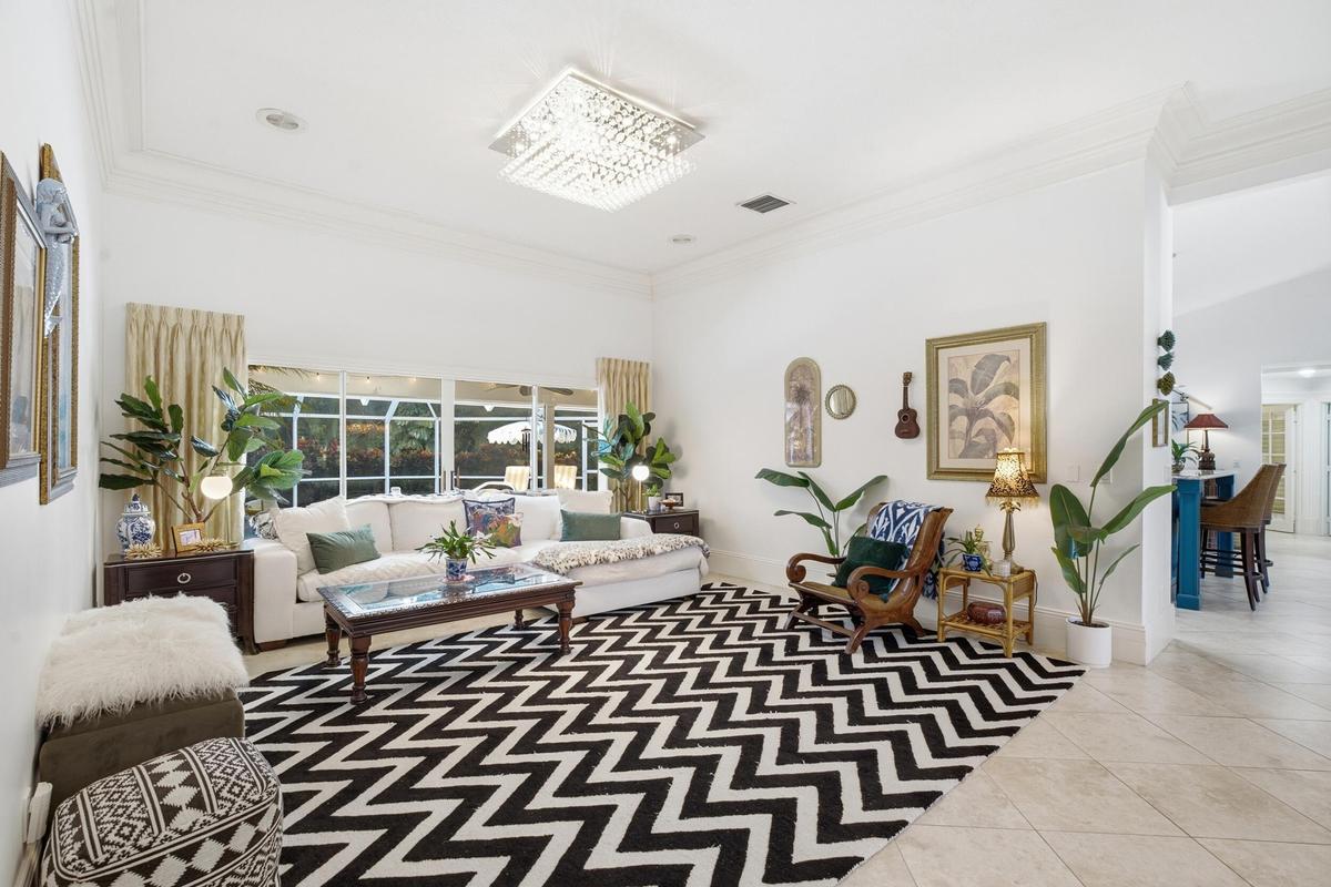 High-ceiling interior featuring crown molding, large-format tile flooring, oversized sliding glass doors, and a decorative crystal flush-mount light f
