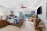 Tray ceiling, neutral tile flooring, ceiling fan with palm-style blades, and floor-to-ceiling glass sliding doors with screen enclosure
