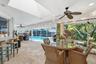Screened-in lanai featuring stone tile flooring, a built-in stone countertop pass-through, a vaulted ceiling with skylights, multiple ceiling fans, an