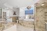 Bathroom featuring a jetted soaking tub set within a stone-tiled surround, a walk-in shower with diamond-pattern stone tile, a stone-surfaced vanity, 