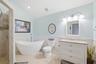 Bathroom featuring a freestanding soaking tub, a vanity with a light-toned countertop and integrated sink, a walk-in tiled shower, white beadboard wai