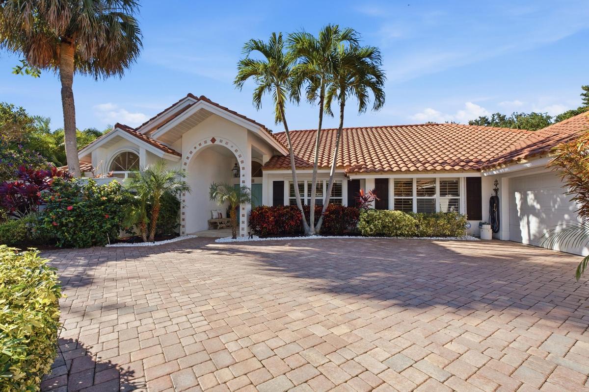 Stucco exterior featuring a clay tile roof, arched entryway with decorative detailing, paver driveway, and mature palm trees
