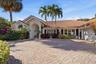 Stucco exterior featuring a clay tile roof, arched entryway with decorative detailing, paver driveway, and mature palm trees