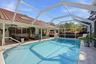 Screen-enclosed swimming pool with built-in stairs, tile pool deck, and clay tile roof