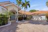 Stucco exterior featuring a tiled roof, arched entryway with decorative detailing, paver driveway, and mature landscaping