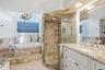 Spa-inspired primary bathroom featuring a soaking tub with tile surround, walk-in shower with glass enclosure and stone-look tile walls, dual vanity w