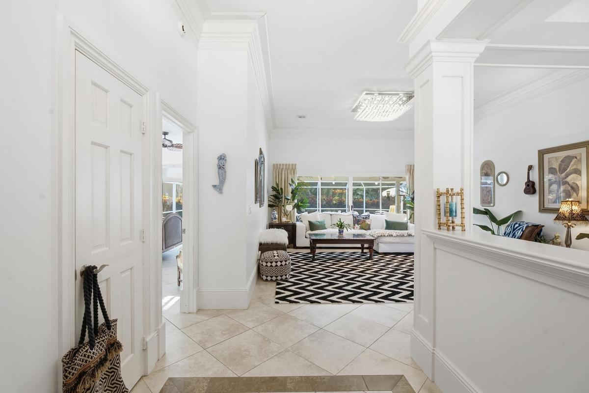 Entryway featuring large-format tile flooring, high ceilings with crown molding, square columns, and a statement crystal flush-mount light fixture