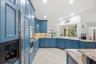 Kitchen featuring custom blue shaker-style cabinetry, natural stone countertops, tile flooring, built-in double wall ovens, and recessed lighting