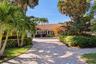 Exterior facade featuring a Spanish-style tiled roof, paver driveway, and mature tropical landscaping