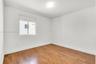 Room featuring wood-finish flooring, white walls, and a single-pane window with a roller shade, illuminated by a flush-mount ceiling light