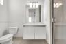 Floating vanity with an integrated countertop, large frameless wall-mounted mirror, three-light frosted glass fixture, and glass-enclosed shower