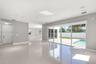 Large format tile flooring, recessed lighting, ceiling-mounted speakers, and expansive floor-to-ceiling glass sliding doors opening to a concrete pati