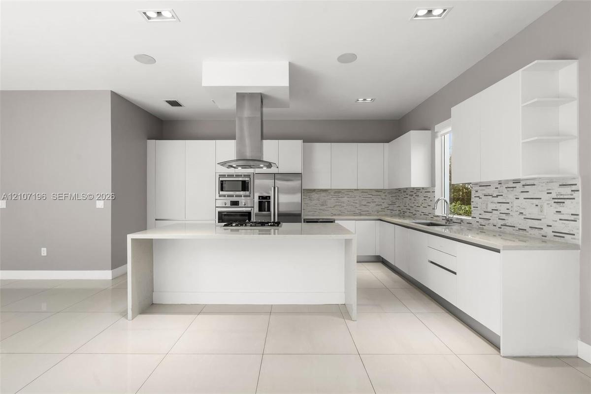 Kitchen featuring flat-panel cabinetry, a central island with a waterfall countertop, stainless steel appliances, a linear-patterned backsplash, and l