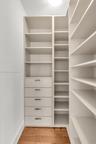Customized built-in storage system featuring floor-to-ceiling shelving, five soft-close drawers with metallic pulls, and wood-finish flooring