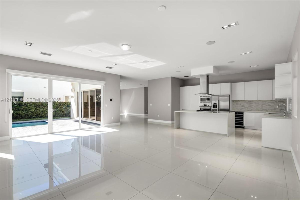 Open-concept space featuring polished tile flooring, white slab-front cabinetry, a kitchen island with stone-surface countertop, built-in stainless st