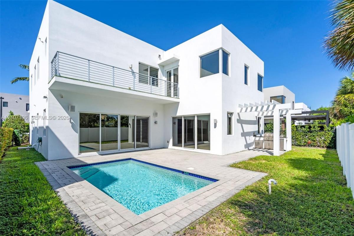 Modern two-story exterior featuring smooth white stucco siding, second-level balcony with horizontal metal railing, in-ground swimming pool, stone-pav