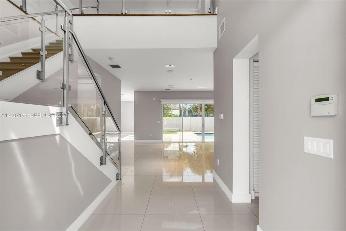 Open-concept foyer featuring oversized light-toned tile flooring, a glass-panel staircase railing, and double-height ceilings