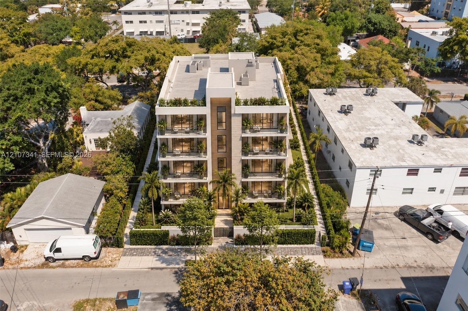 Multi-story residential building featuring a stone-clad facade, private balconies on each level, floor-to-ceiling windows, and landscaped perimeter he