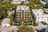 Multi-story residential building featuring a stone-clad facade, private balconies on each level, floor-to-ceiling windows, and landscaped perimeter he