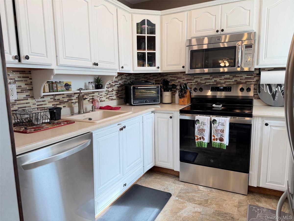 White cabinetry with black hardware, mosaic tile backsplash, stainless steel appliances, and a built-in microwave