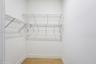 Walk-in storage space featuring multi-tiered white wire shelving, integrated hanging rods, and wood-finish flooring