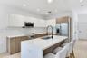 Kitchen featuring flat-panel two-tone cabinetry, stone-surface countertops, a center island with an integrated sink and gooseneck faucet, stainless st