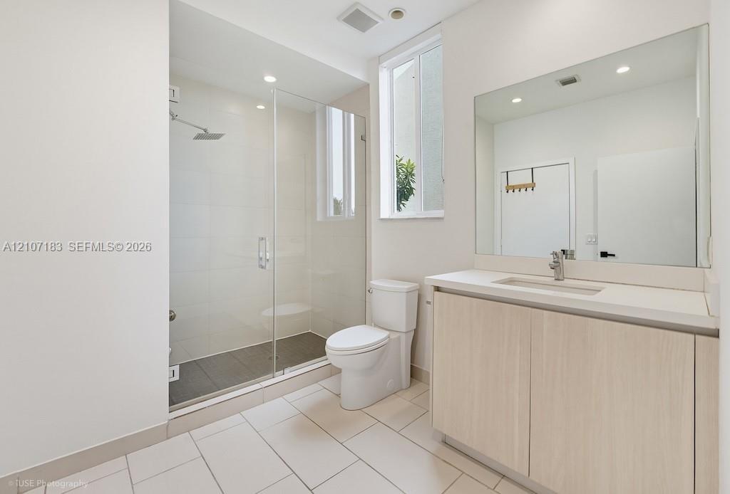 Bathroom featuring a glass-enclosed walk-in shower with a rain-style showerhead, wood-finish vanity with a rectangular basin, light-toned tile floorin