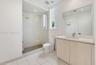 Bathroom featuring a glass-enclosed walk-in shower with a rain-style showerhead, wood-finish vanity with a rectangular basin, light-toned tile floorin