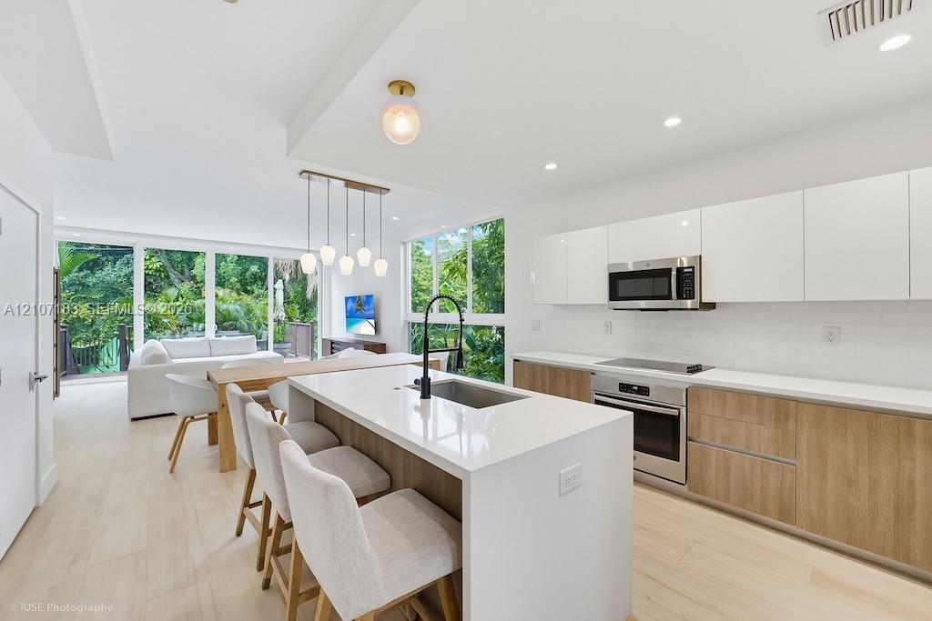 Modern kitchen featuring a central island with a quartz countertop, white flat-panel upper cabinetry, wood-finish lower cabinetry, integrated stainles