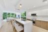 Modern kitchen featuring a central island with a quartz countertop, white flat-panel upper cabinetry, wood-finish lower cabinetry, integrated stainles